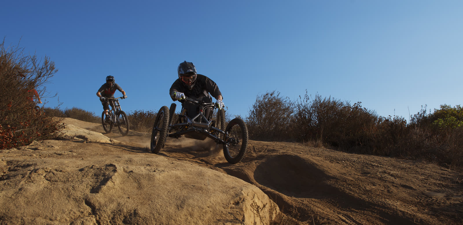 Two adaptive riders descending a desert trail at golden hour